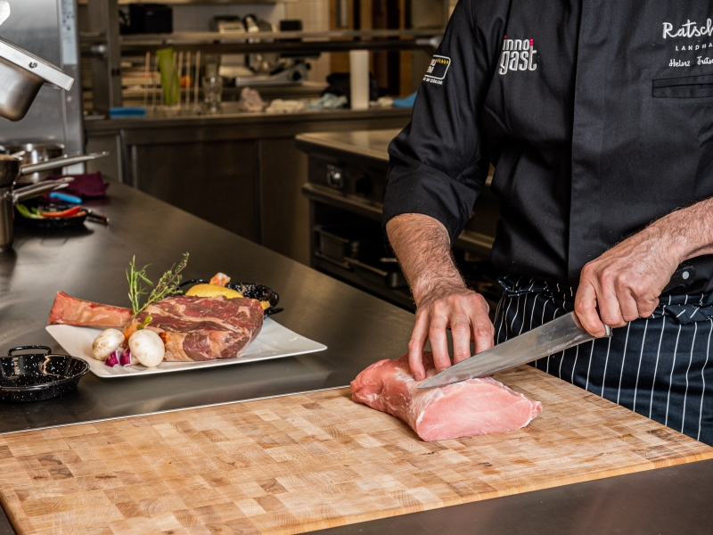 Portionieren von Fleisch am hölzernen Hack- und Schneideblock (bündig eingelassen in Edelstahl-Arbeitsfläche)