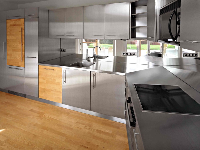 Haushaltsküche in Edelstahl inklusive Wandverbau und Hochschränken; teilweise mit Holzfronten als Akzent